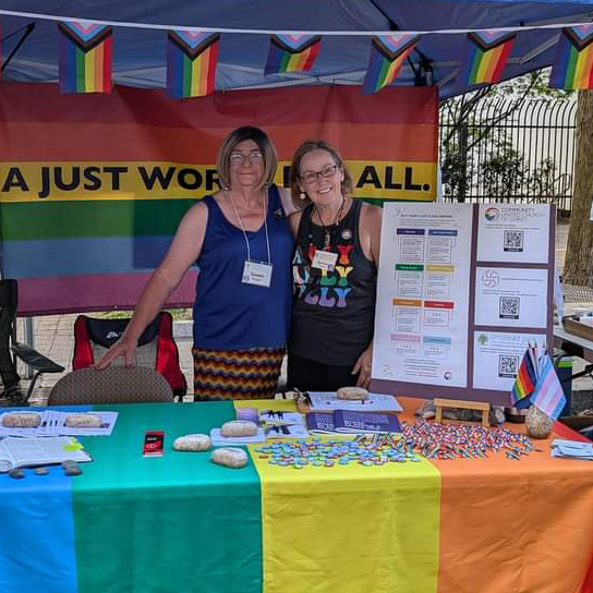 Covenant Partners running the UPUCC table at Out Raleigh with pride flags and a banner reading "A Just World for All."